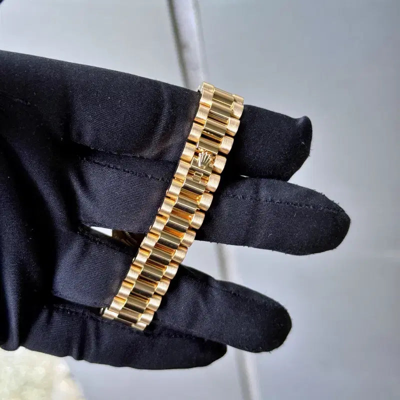 Gold watch bracelet held by a gloved hand against a neutral background