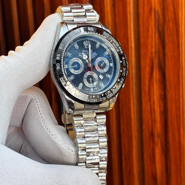 Silver watch with a blue face held by a gloved hand against a wooden background