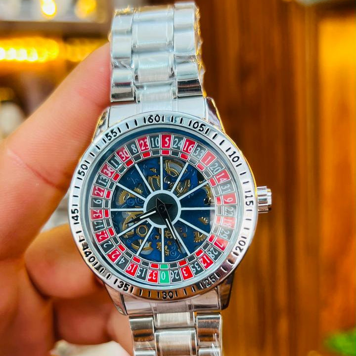 Silver watch with a colorful face held by a hand against a blurred background