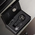 Black watch with accessories in a branded box on a gray surface